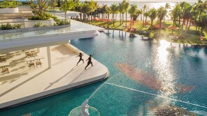 Área de piscina en un resort, con vista despejada al océano, sillas de descanso y palmeras.