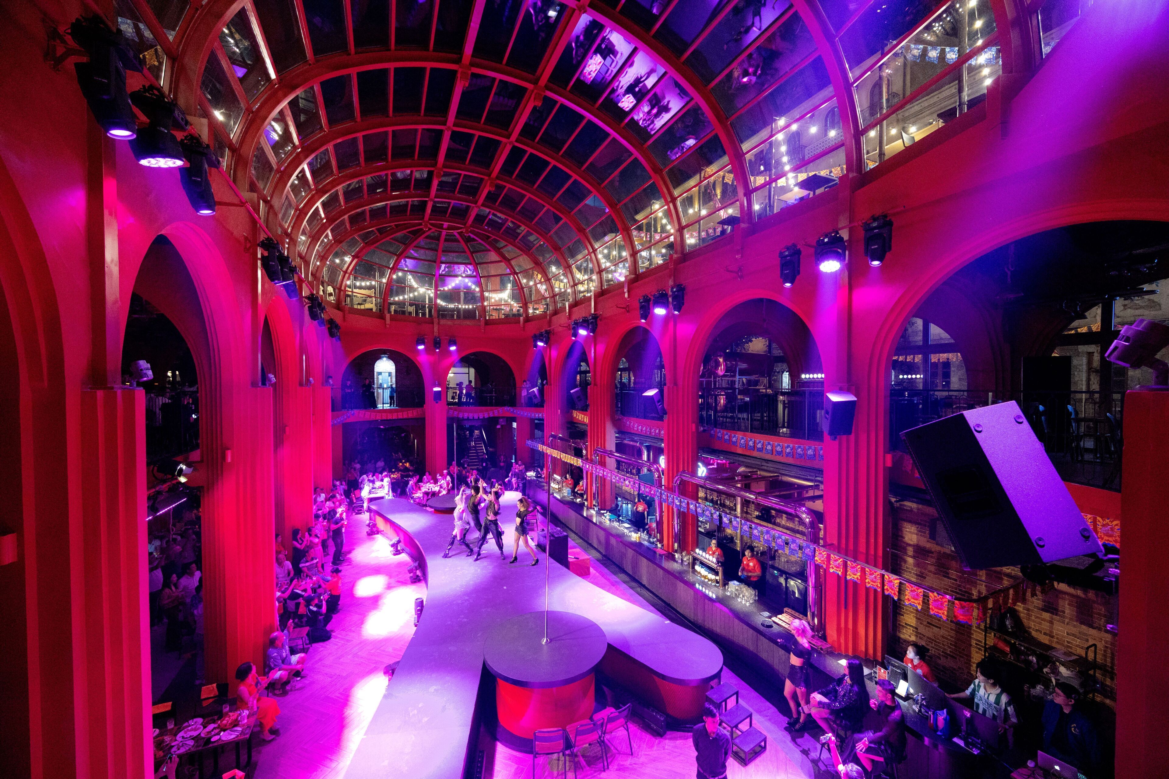 A spacious atrium with a high ceiling and arched columns, featuring a central open area with seating and a stage for performances.