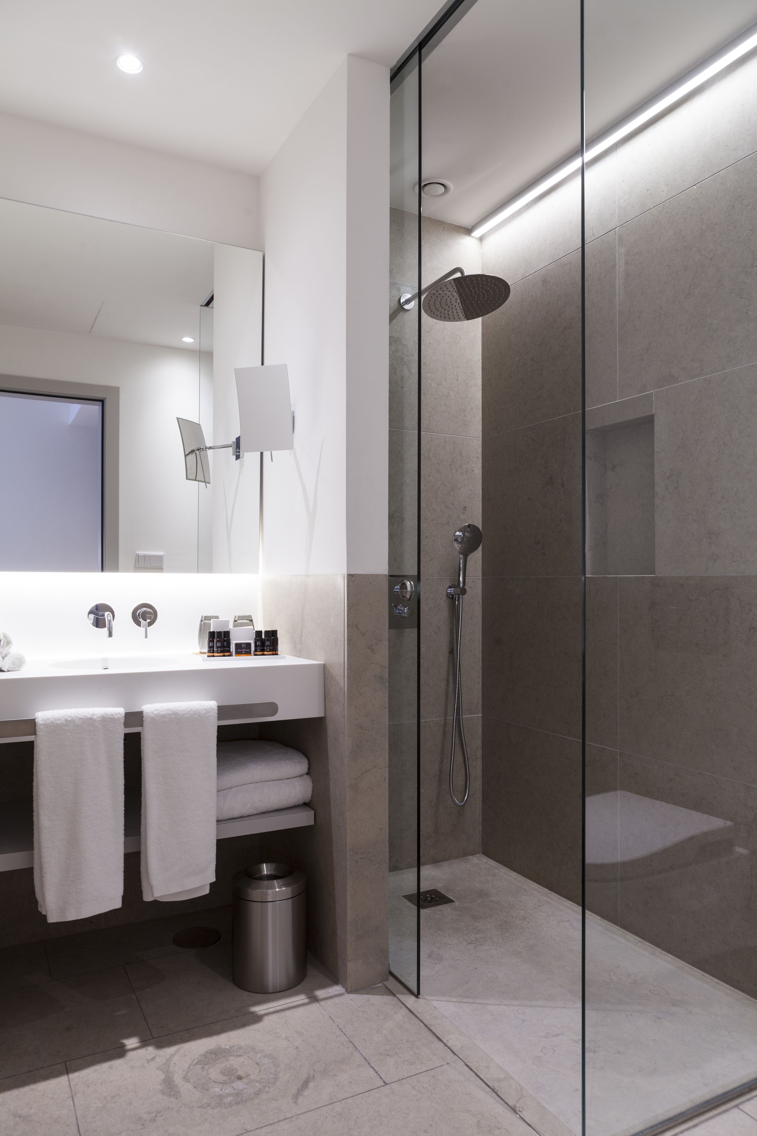 Un baño moderno con ducha envuelta en vidrio, un espejo grande y un lavamanos con toallero.