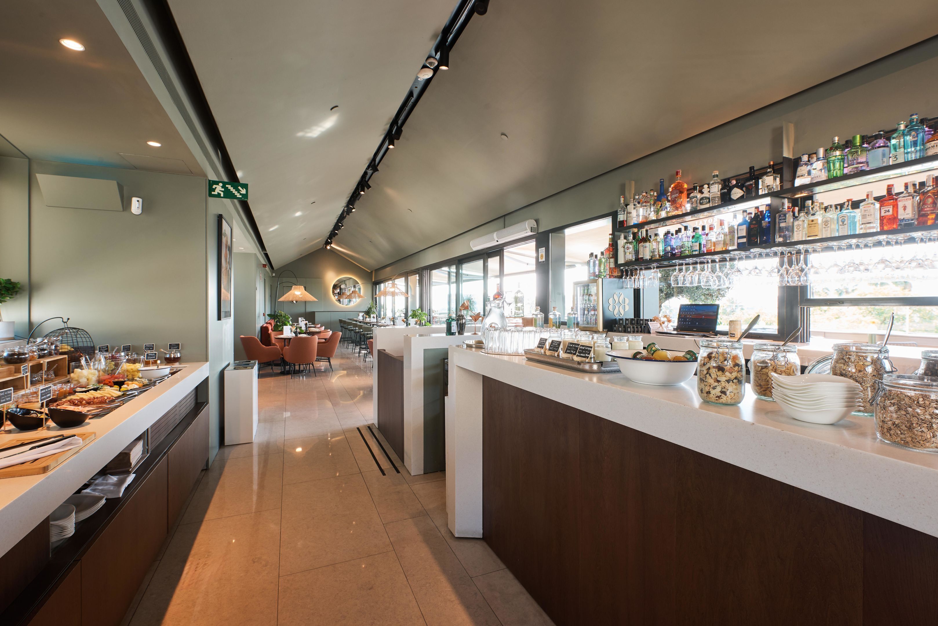 A modern hotel lobby with a buffet area, seating arrangements, and a bar with a variety of beverages.