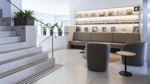 Un vestíbulo moderno con una escalera, una zona de estar y una pared decorada con libros y plantas.