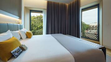 Una habitación de hotel con una cama grande, cabecera, ventana con vistas a la ciudad y balcón con barandilla.