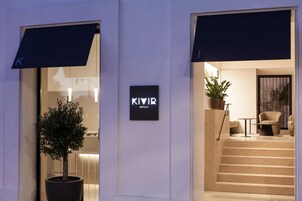 Ein moderner Hotelzugang mit einem Blumentopf, einem Schild mit der Aufschrift 'KIVIR SEVILLA' und einer Treppe, die zum Eingang führt.