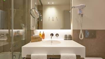 A modern bathroom with a glass-enclosed shower, a white sink with a mirror, and a hairdryer on the wall.