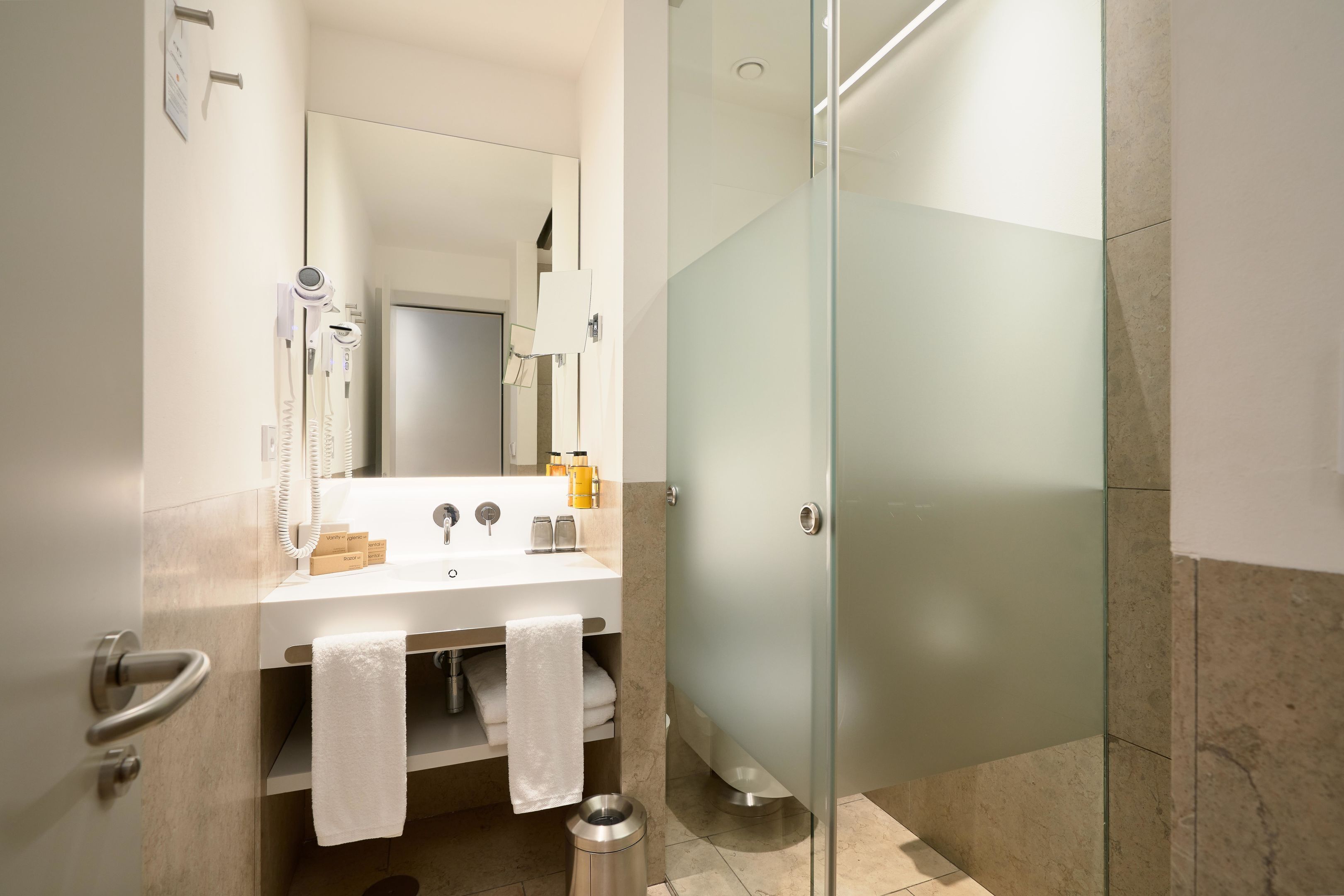 A modern bathroom with a glass shower enclosure, a white sink with a mirror, and a towel rack.