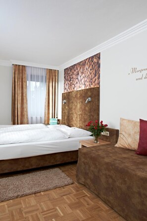 A hotel room with a bed, a wooden headboard, a sofa, a small table, and a wall with a text decoration. - Biergasthof Riedberg (Ried im Innkreis)