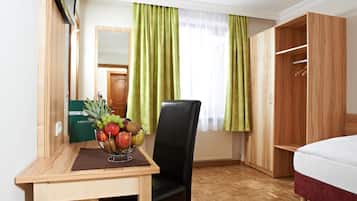 Een hotelkamer met een houten bureau, een stoel, een bed, een kledingkast en een raam met groene gordijnen.