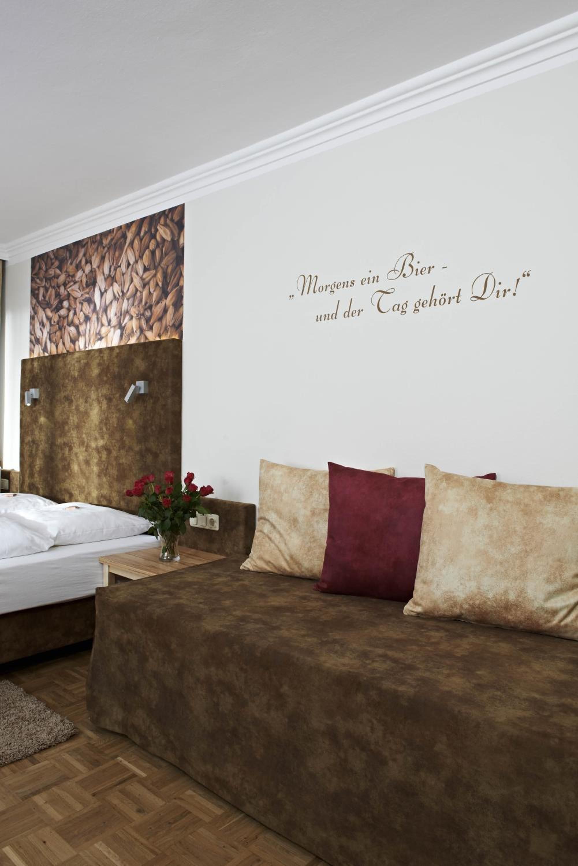 Een slaapkamer met een bed, een bruine bank, een muur met een citaat en een schilderij van zaden.