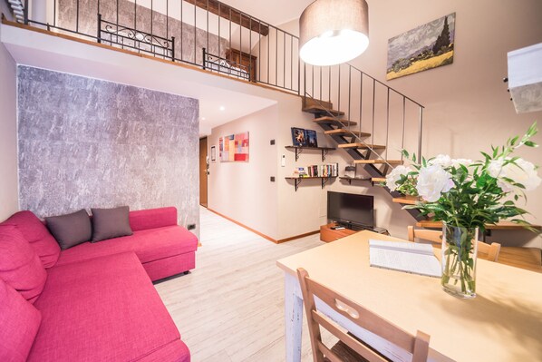 Un salon moderne avec un canapé rouge, une table à manger en bois et un escalier menant à un niveau supérieur.