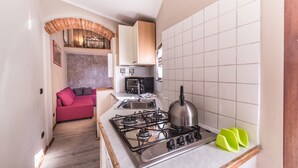 A compact kitchen with a gas stove, a toaster, and a sink. There is a red sofa in the adjacent living area.