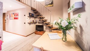 A modern interior with a wooden staircase, a dining area with a table and chairs, and a bookshelf.