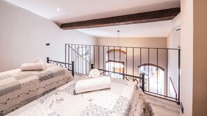 A bedroom with two beds, a wooden ceiling, a balcony with a railing, and a view of the outside.