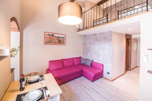 Un salon moderne avec un canapé d’angle rose, une table à manger avec de l’argenterie et des bouteilles de vin, et un escalier doté d’une rampe en métal.