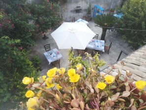 Un espace extérieur aménagé en terrasse, avec des tables et des chaises, entouré de verdure et de plantes en pot.
