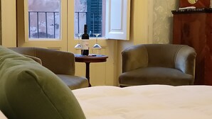 A hotel room with a bed, two armchairs, a small table with a wine bottle and glasses, and a window with a view of the outside. - Residenza Donnafugata B&B (Ragusa)