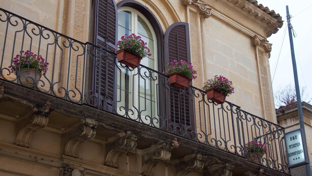 A building facade with ornate balconies, flower boxes, and a sign indicating the name and address. - Residenza Donnafugata B&B (Ragusa)