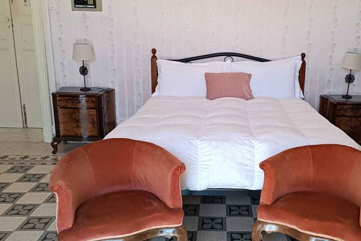 Ein ordentlich eingerichtetes Schlafzimmer mit einem großen Bett, zwei Nachttischen mit Lampen, einem kleinen Sofa und einem gemusterten Teppich.
