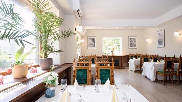 A dining area with tables set for a meal, chairs, and potted plants.