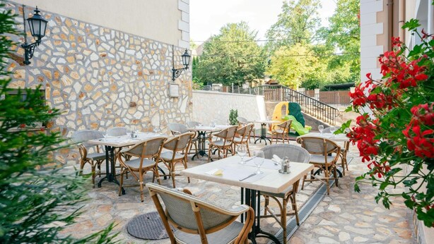 Un patio al aire libre con suelo de piedra, mobiliario de mimbre y pared de piedra.