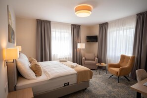 Habitación de hotel con cama, dos sillones, una mesita, televisor y un cuadro en la pared.