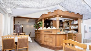Una zona de bar con mobiliario de madera y una barra, rodeada por un comedor con sillas y una mesa.