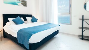 A bedroom with a large bed, a view of the sea through a window, and a painting on the wall. - Almog Beach (Haifa)