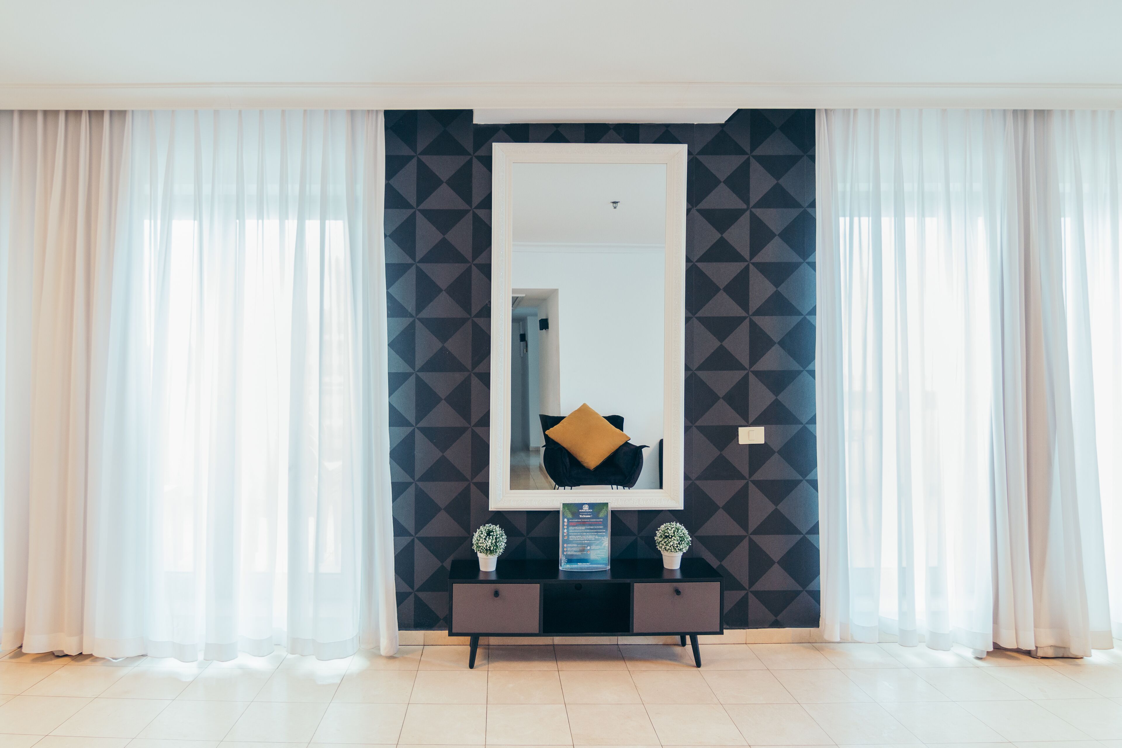 Una habitación moderna con un espejo grande, una consola negra con dos plantas en macetas y paredes con un estampado geométrico.