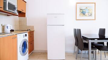 Cocina compacta con lavadora, microondas y refrigerador. Cuenta con una mesa de comedor con sillas y un cuadro en la pared.