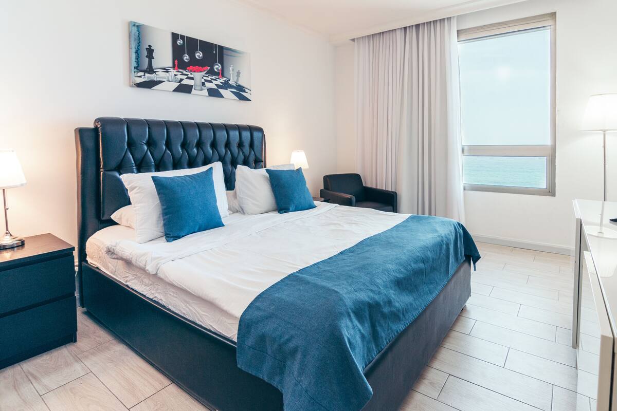 A hotel room with a large bed, a chair, a desk, and a window with a view.