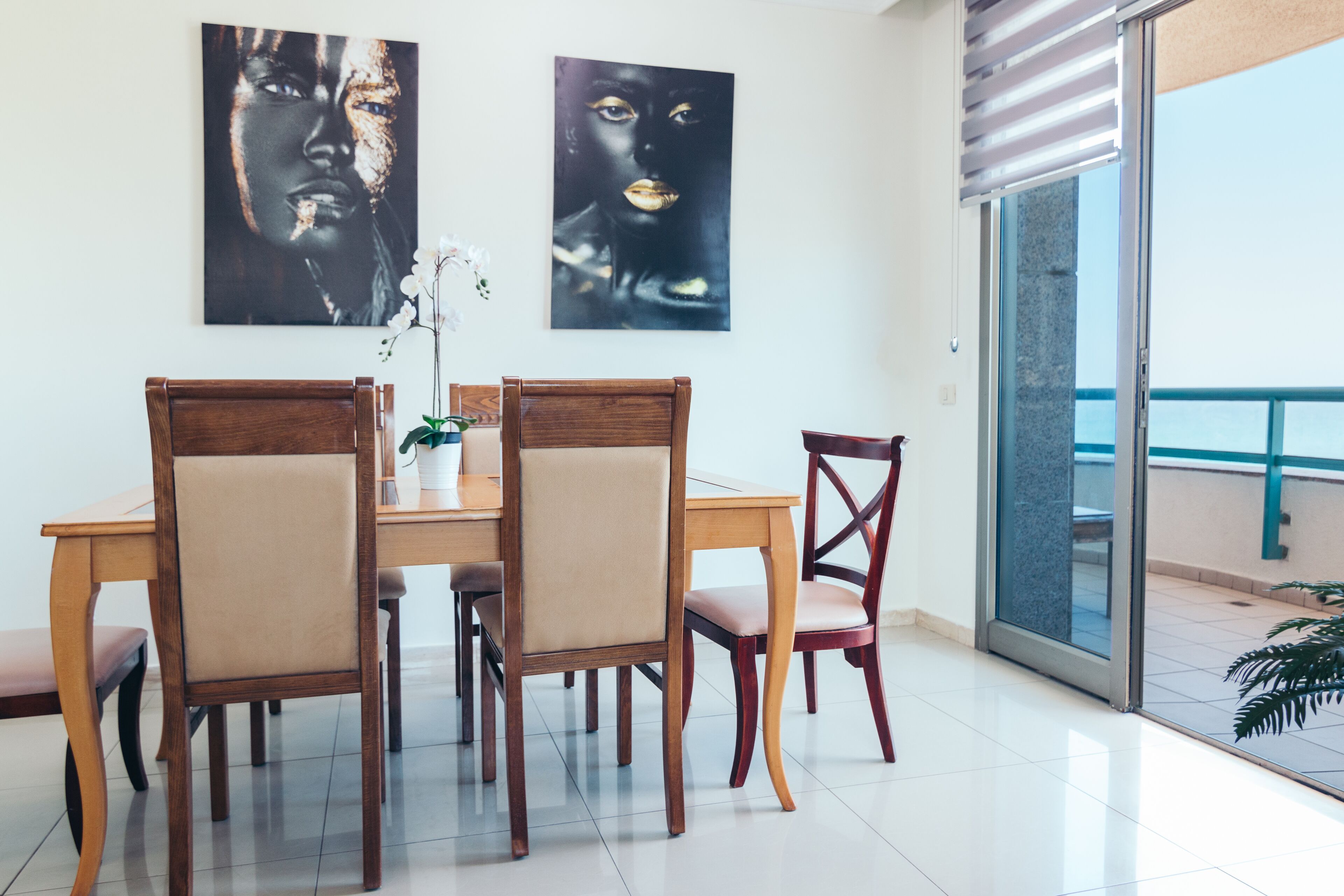A dining area with a wooden table and chairs, two wall-mounted artworks, and a sliding glass door leading to an outdoor balcony.