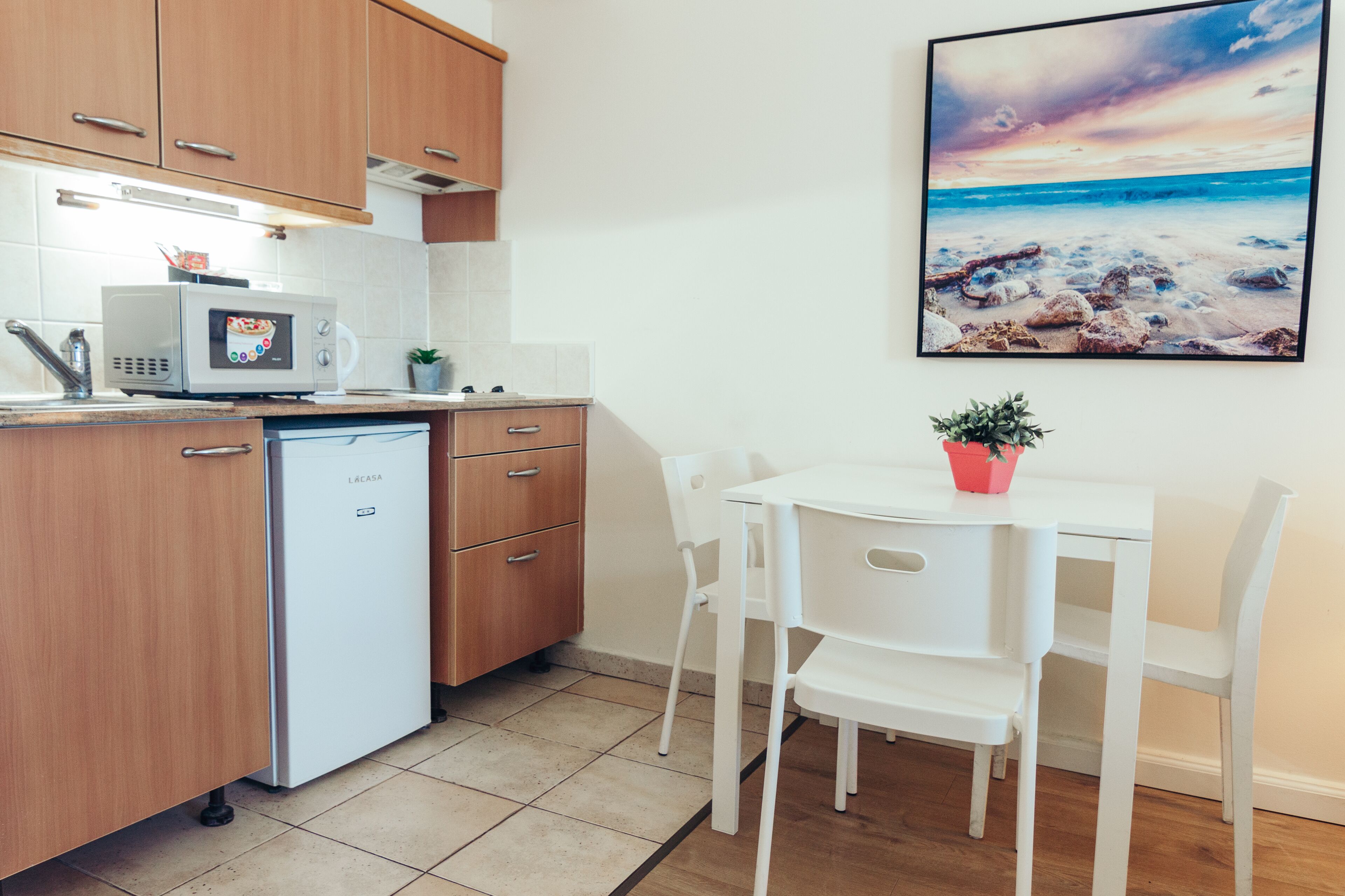 Une cuisine compacte avec des meubles en bois, un réfrigérateur blanc, un four à micro-ondes et une petite table à manger avec des chaises.
