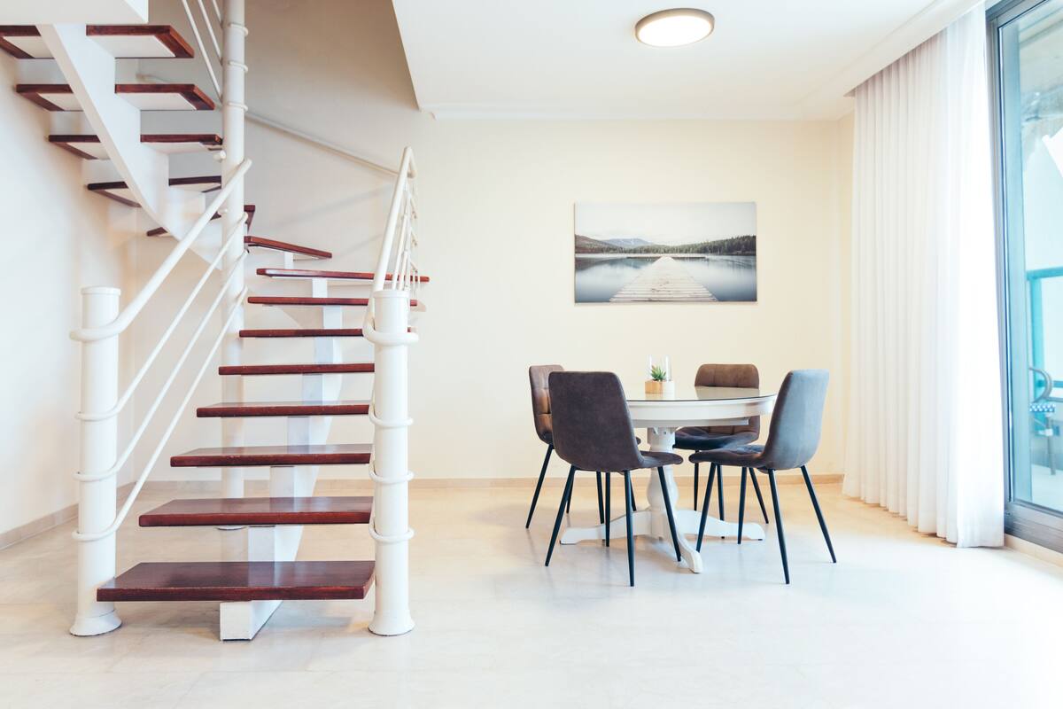 A modern interior with a spiral staircase, a dining area with a table and chairs, and a large window with a view.