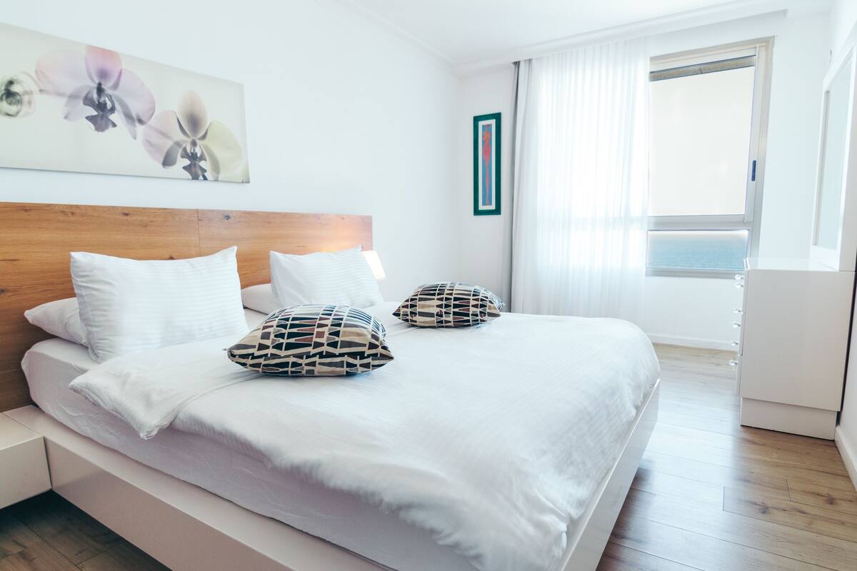 A modern hotel room with a large bed, white bedding, and decorative pillows.