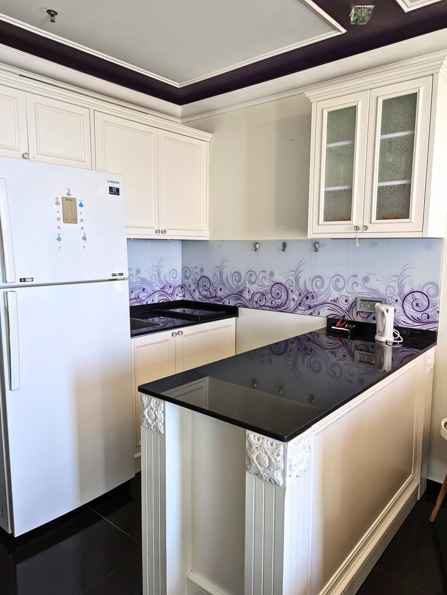 A kitchen with white cabinets, a black countertop, and a decorative backsplash.