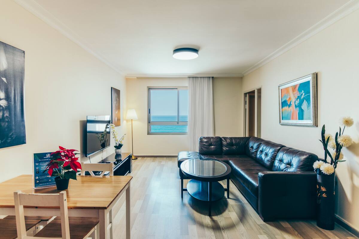 A modern living room with a leather sofa, a round coffee table, a wooden dining table, and a TV.