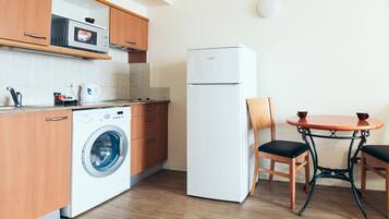 A compact kitchen with wooden cabinets, a washing machine, a refrigerator, and a small dining table with chairs.