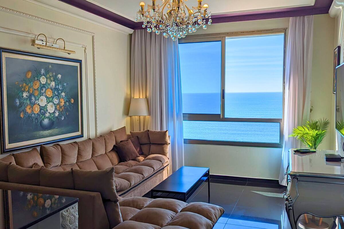 A living room with a sofa, a coffee table, and a view of the sea.