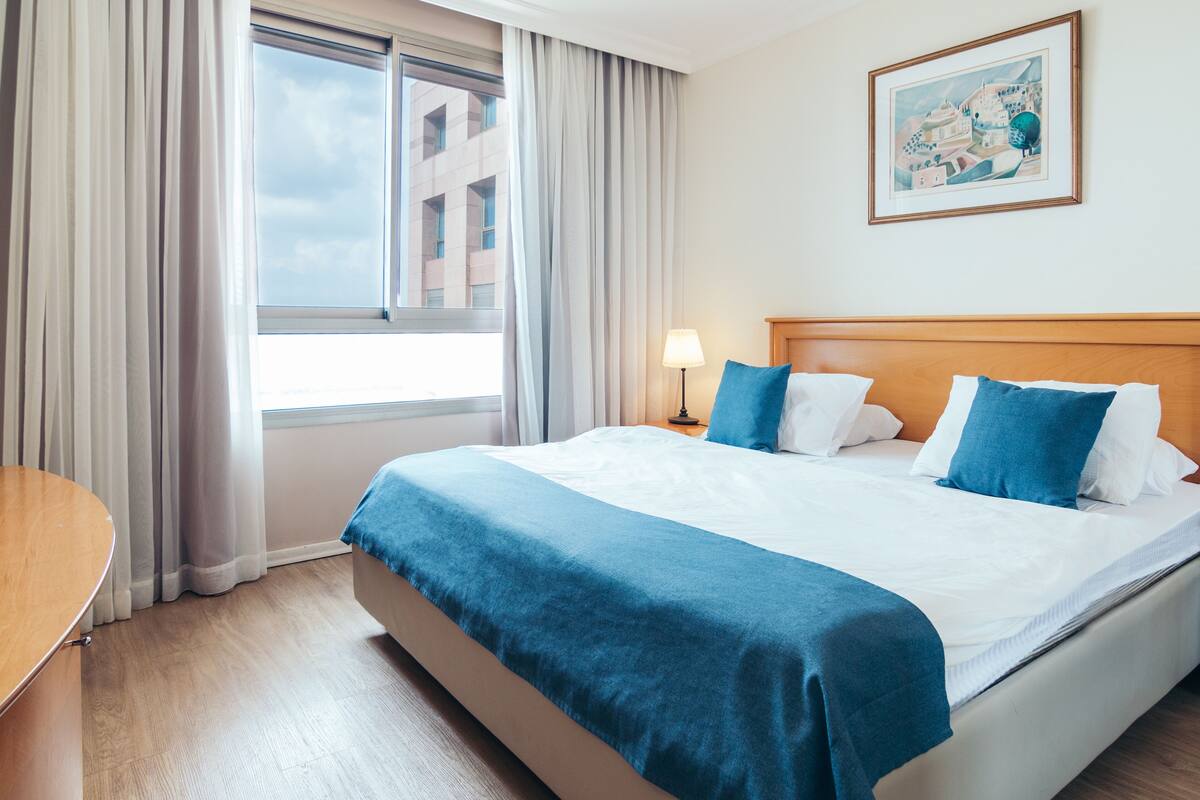 A hotel room with a large bed, a bedside table, a lamp, and a window with curtains.