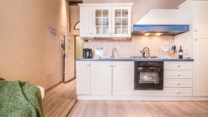 Una cocina compacta con muebles blancos, cocina a gas, cafetera y lavamanos.