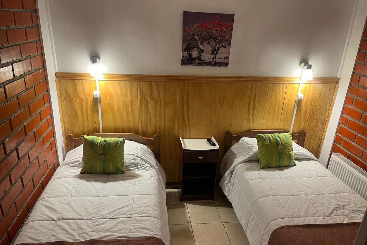 Ein Zimmer mit zwei Betten, jeweils mit Holz Kopfteilen und weißer Bettwäsche. Es gibt zwei Nachttische mit Lampen, einen kleinen Beistelltisch und eine Heizung.