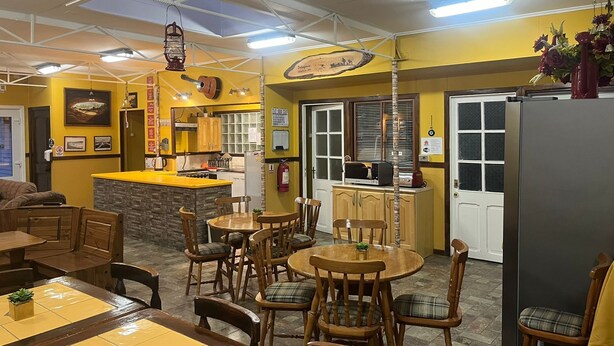 A cozy restaurant with a yellow and brown color scheme, featuring a bar area, dining tables, and wooden chairs. - Hostal Maipu Street (Punta Arenas)