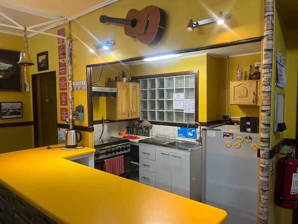 A kitchen with yellow walls, a guitar hanging above the counter, and a coffee station.