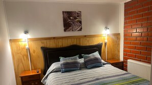 A bedroom with a wooden headboard, two bedside tables, a bed with striped bedding, and a brick wall. - Hostal Maipu Street (Punta Arenas)