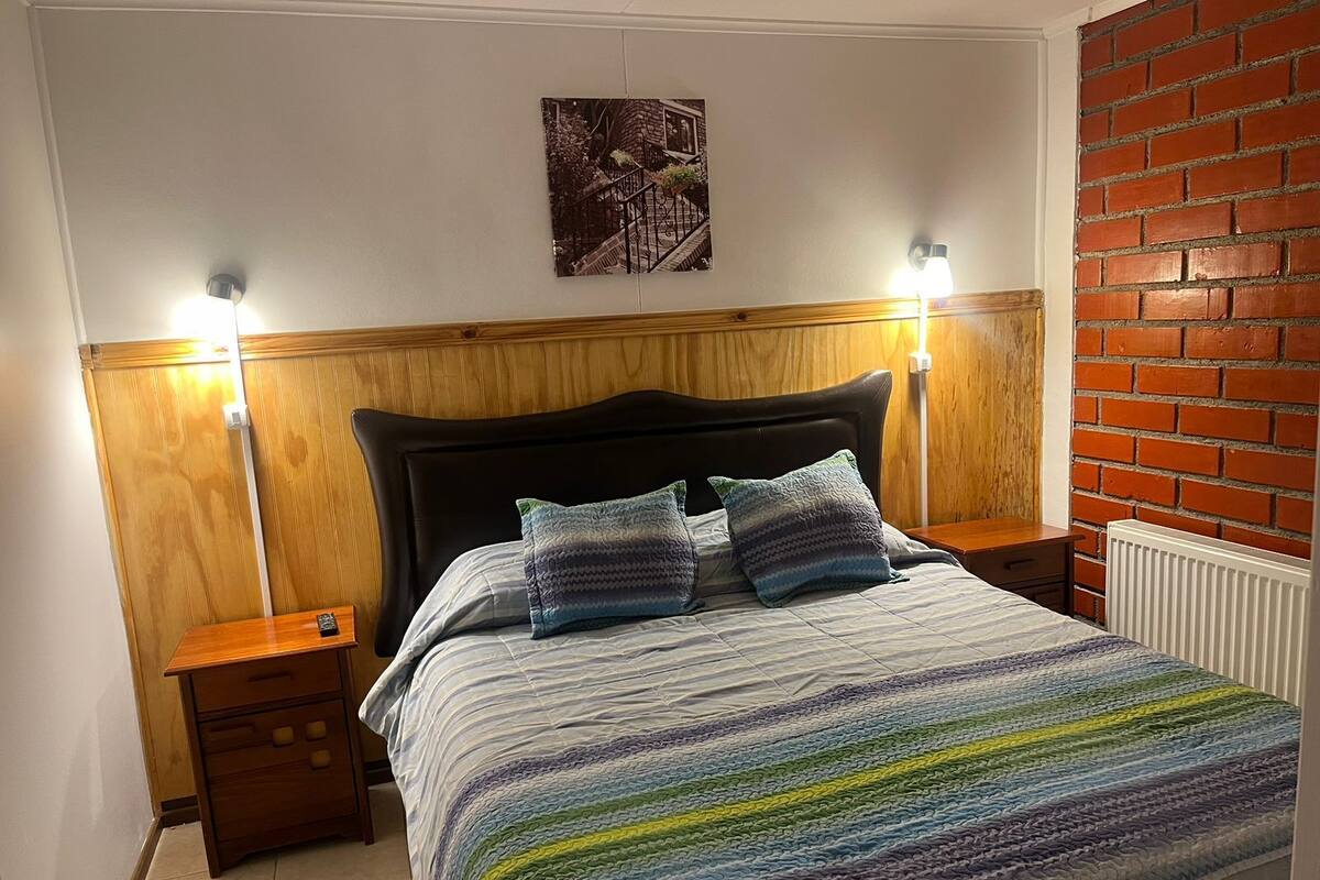 Ein Schlafzimmer mit Holzkopfteil, zwei Nachttischen, einem Bett mit gestreifter Bettwäsche und einer Ziegelwand.