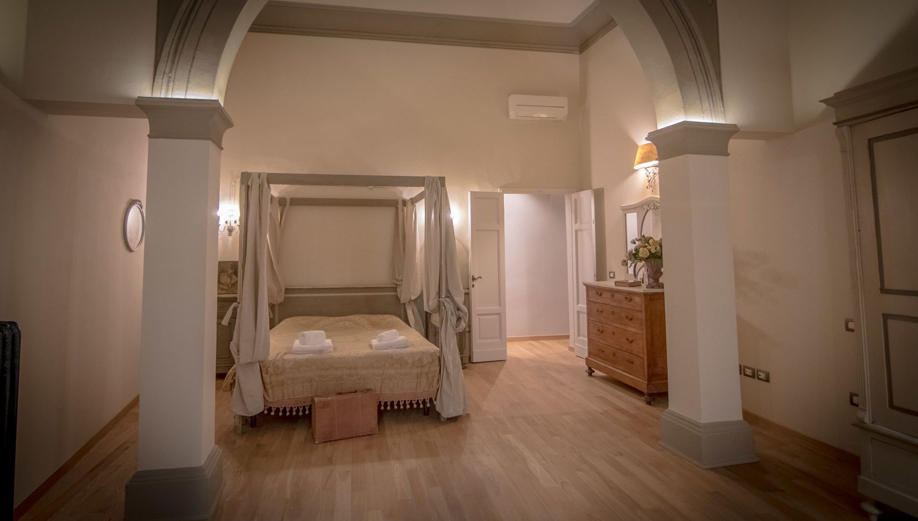 A bedroom with a four-poster bed, a wooden dresser, and a door leading to another room.