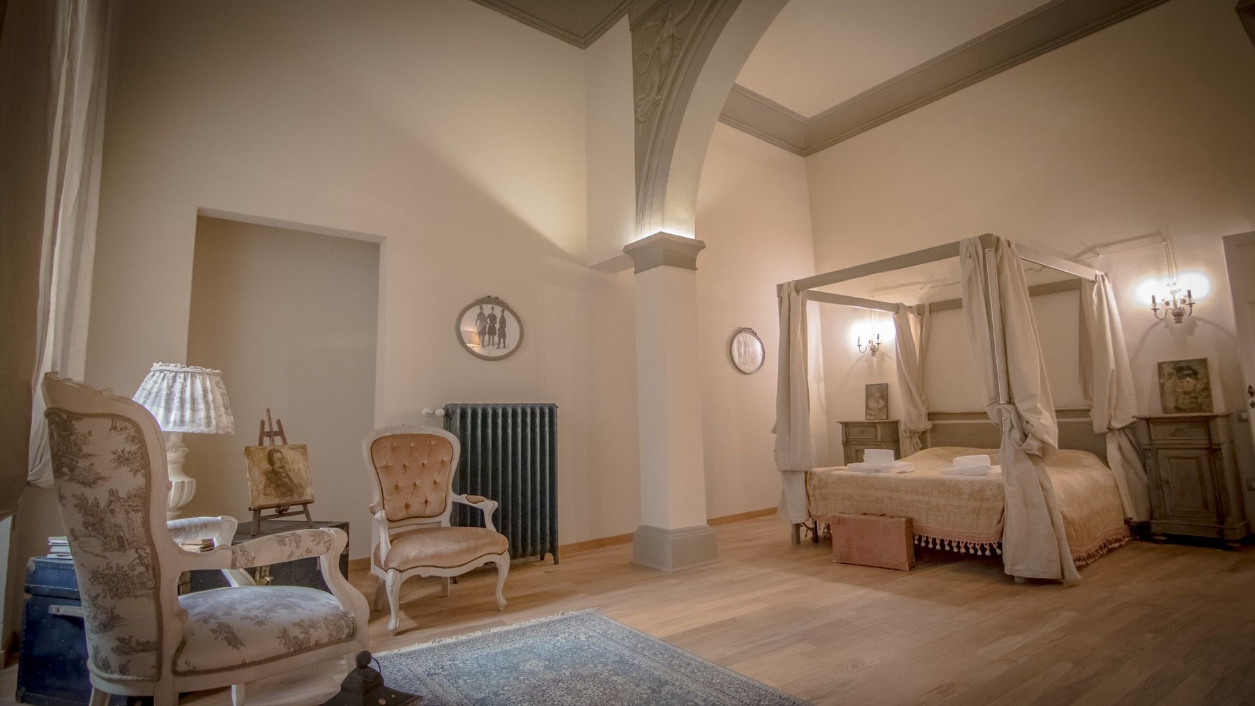 Un dormitorio con cama con dosel, una zona de estar con una silla y una mesa, y un radiador.