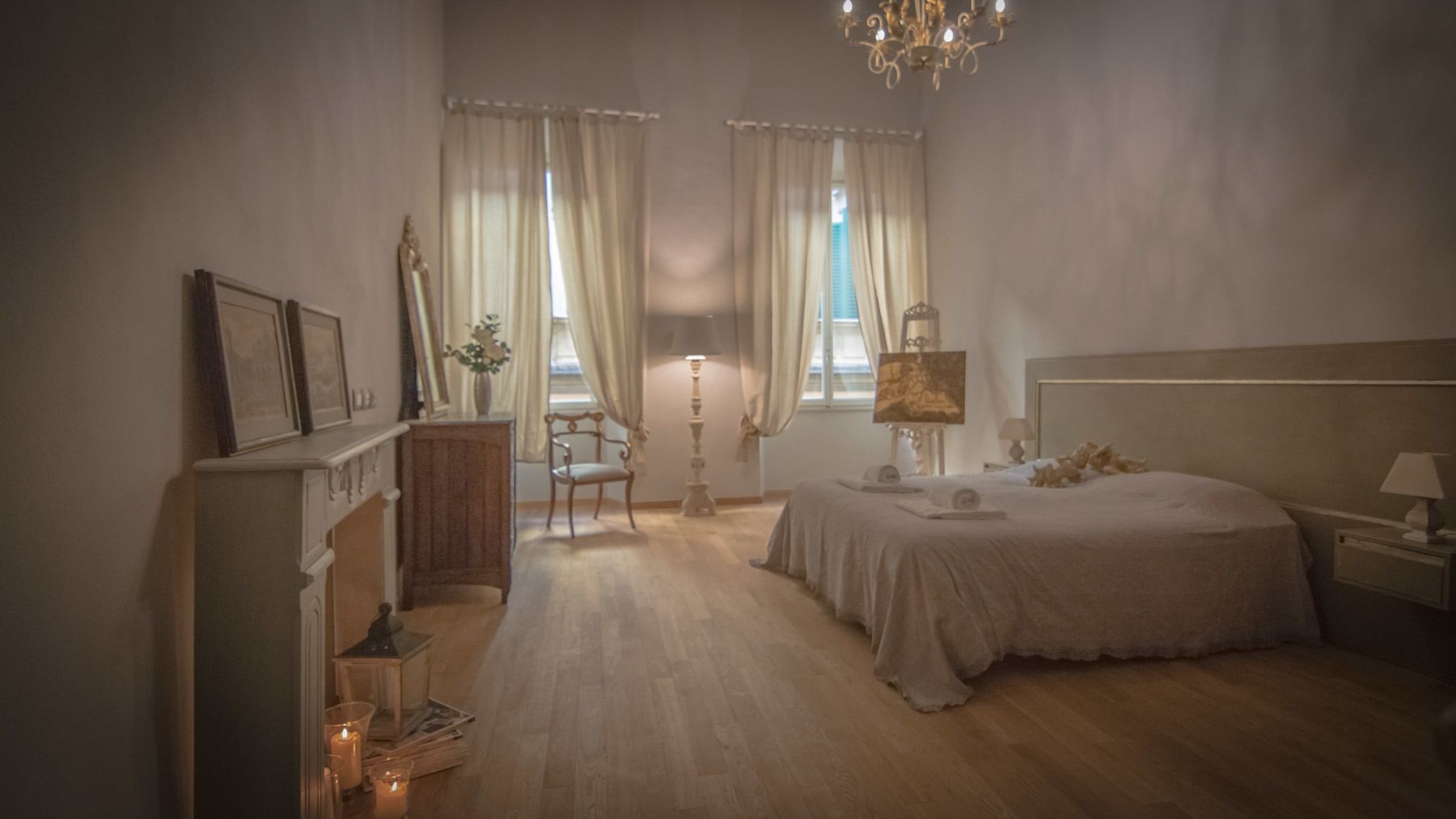 A bedroom with a large bed, a nightstand, a chair, a dresser, and a chandelier.