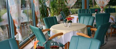 A restaurant with round tables and teal chairs, featuring a view through large windows.