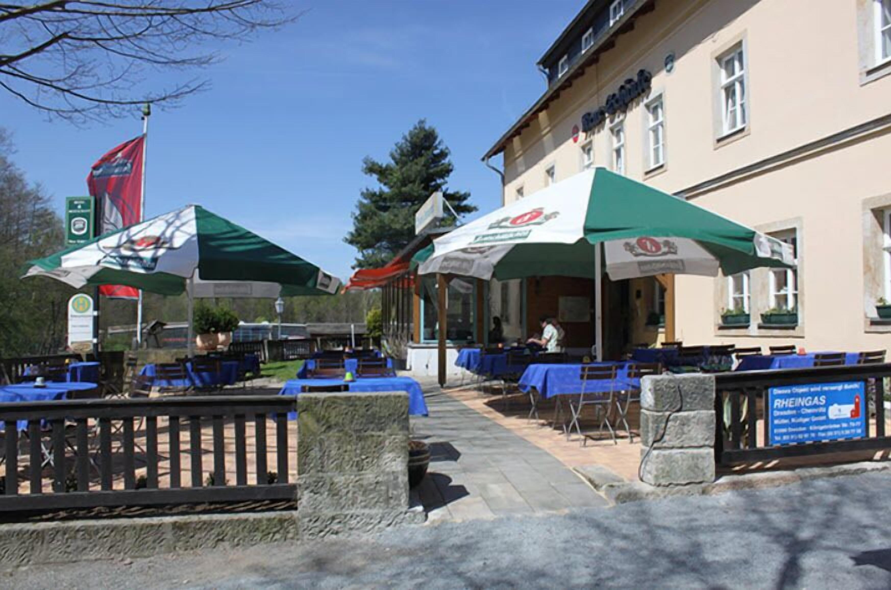 An outdoor seating area with tables and chairs, a stone wall, and a building with a sign.