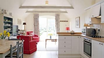 A spacious kitchen with a dining area, featuring a red sofa, a wooden dining table, and a view to the outside.